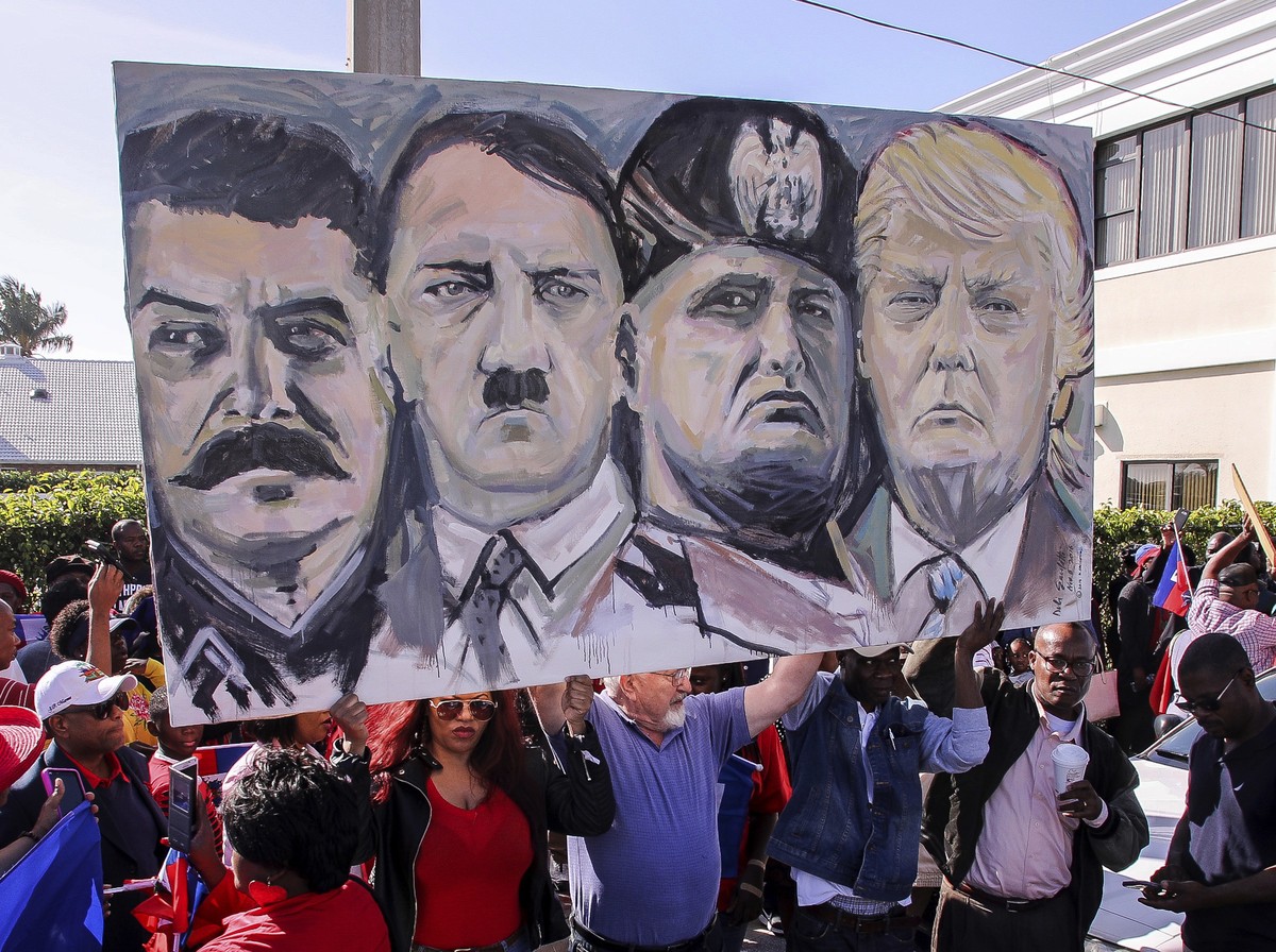Haitian community members hold an image depicting image shows from left, Joseph Stalin, Adolf Hitler, Benito Mussolini and President Donald Trump during a protest near Trump's Mar-a-Lago estate M ...