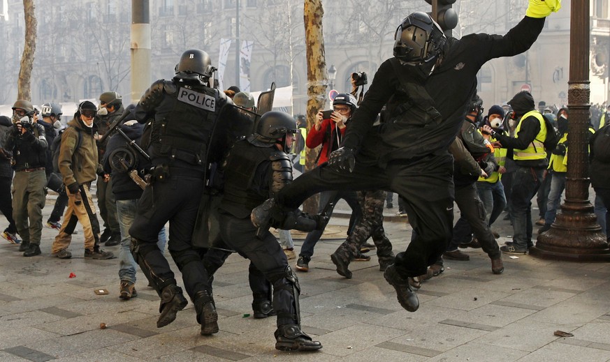 epa07442881 A Yellow Vest protester hits a riot police officer with his leg on the Champs Elysees during the &#039;Act XVIII&#039; demonstration (the 18th consecutive national protest on a Saturday) i ...