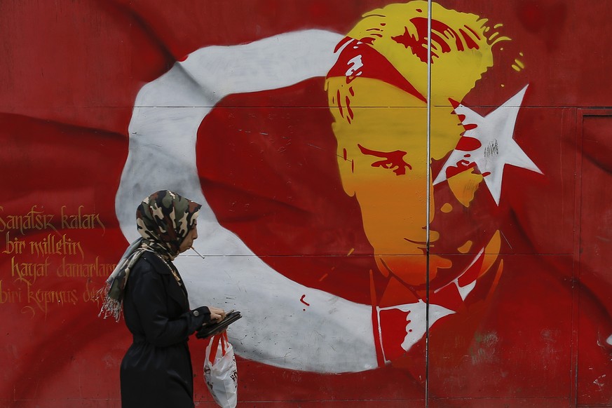 A woman walks past a billboard with a Turkish flag decorated with an image of Turkey&#039;s founder Kemal Ataturk, in Istanbul, Wednesday, April 12, 2017. Turkey is heading to a contentious April 16 r ...