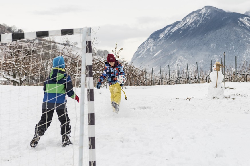 Oscar und Arthur spielen im Neuschnee Fussball neben ihrem Schneemann, am Sonntag, 16. Dezember 2018 in Flanthey VS. In der Nacht auf Sonntag hat es im Mittelwallis reichlich geschneit. (KEYSTONE/Ales ...