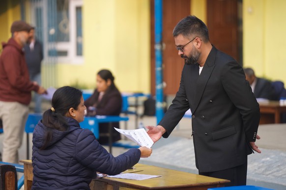 Balendra Shah, right, former mayor of Kathmandu Metropolitan City and prime ministerial candidate of the Rastriya Swatantra Party shows his identity card before casting his vote at a polling station f ...