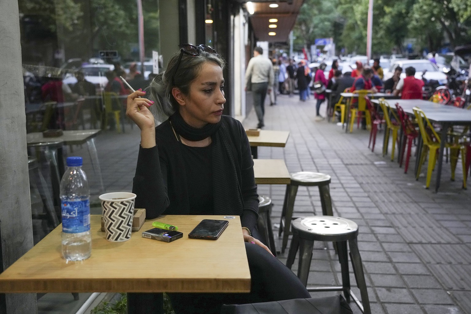 A woman sits in the alfresco dining area of a cafe at Tajrish commercial district without wearing her mandatory Islamic headscarf in northern Tehran, Iran, Saturday, April 29, 2023. More women are cho ...