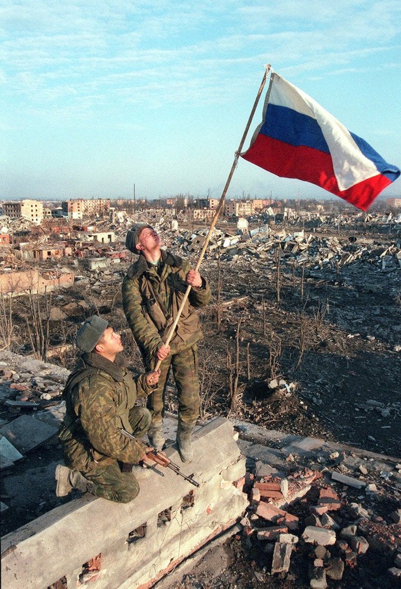 Russian soldiers install a Russian flag over ruins of an apartment building where they say a Chechen sniper was found and killed in Grozny, in this March 1, 2000 photo. Chechnya&#039;s parliament on W ...