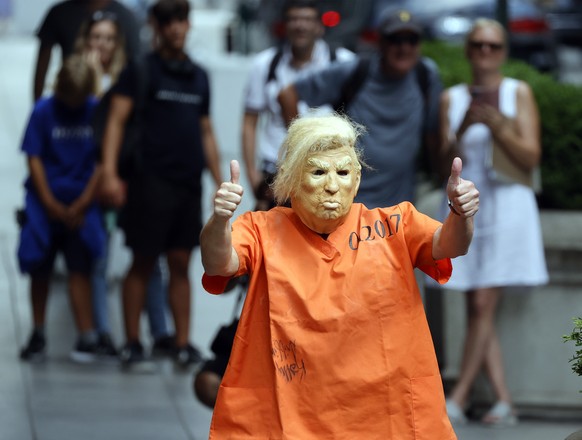 epa10114916 A man wears a mask of former US President Donald Trump and an orange jump suit as he is watched by tourists on Fifth Avenue in front of Trump tower in New York, New York, USA, 10 August 20 ...