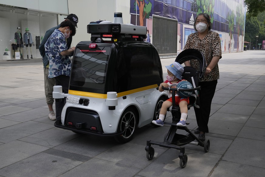 Residents pass by an autonomous surveillance vehicle at a quiet mall area on Monday, May 23, 2022, in Beijing. (AP Photo/Ng Han Guan)