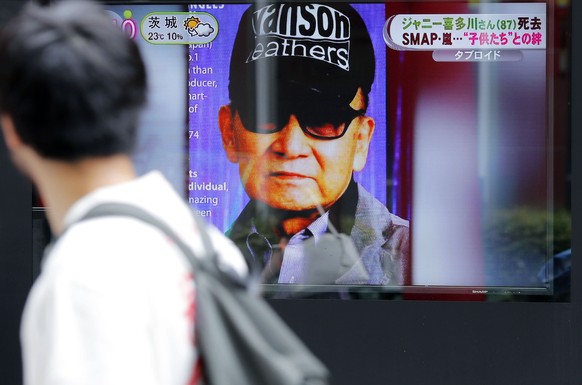 FILE - A passer-by watches a TV news reporting Johnny Kitagawa&#039;s passing away in Tokyo, on July 10, 2019. A growing number of people are alleging sexual abuse by Kitagawa, who ruled over Japanese ...