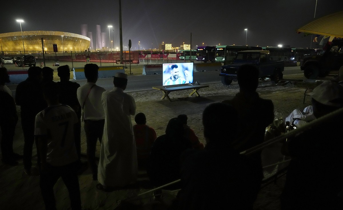 People sit in front of a TV screen as Argentina's Lionel Messi celebrates after scoring the opening goal of the game near the Lusail Stadium in Lusail, Qatar, during the World Cup final soccer ma ...