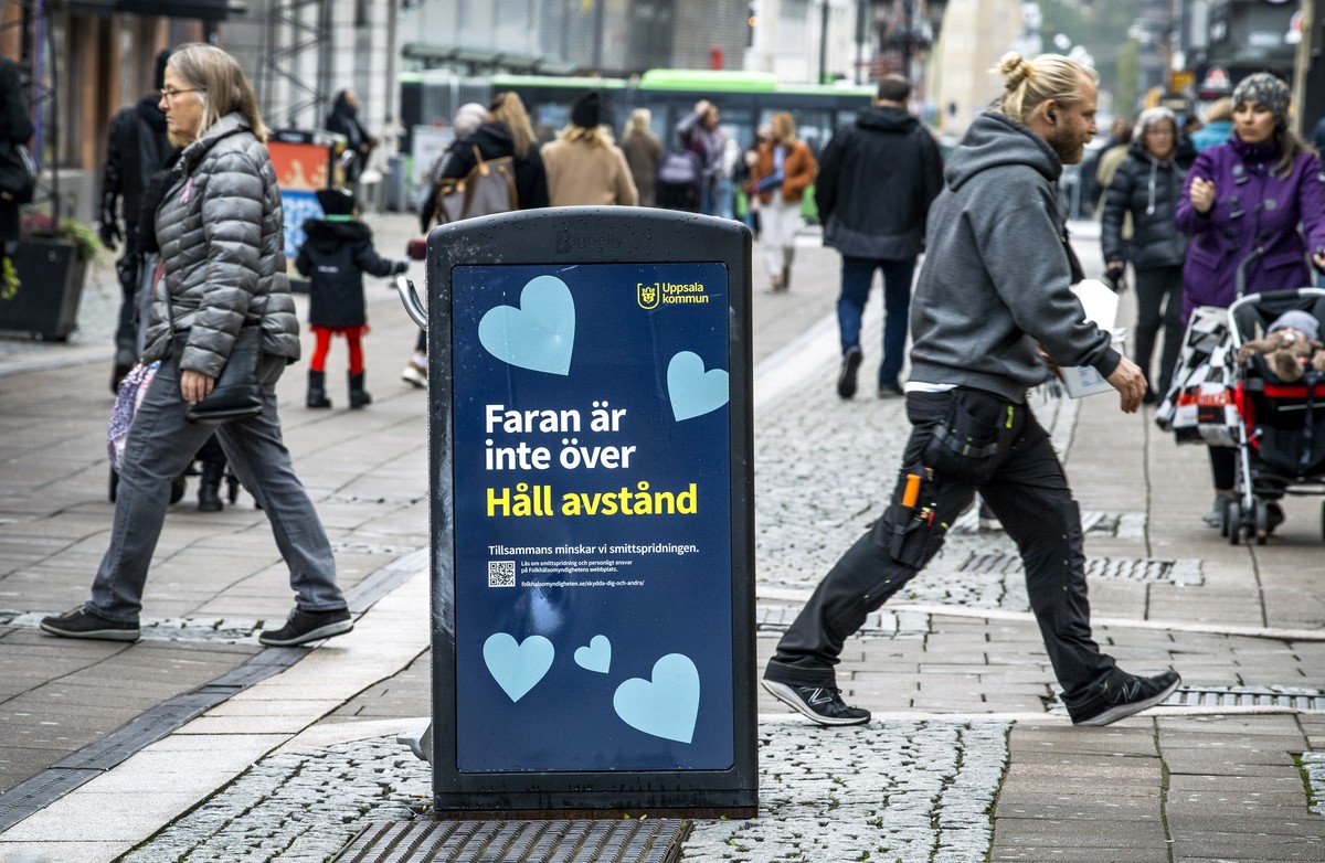 People pass a trash can with a sign reading "The danger is not over - Keep your distance" in a pedestrian street in central Uppsala, Sweden, Wednesday, Oct. 21, 2020. Uppsala, a university c ...