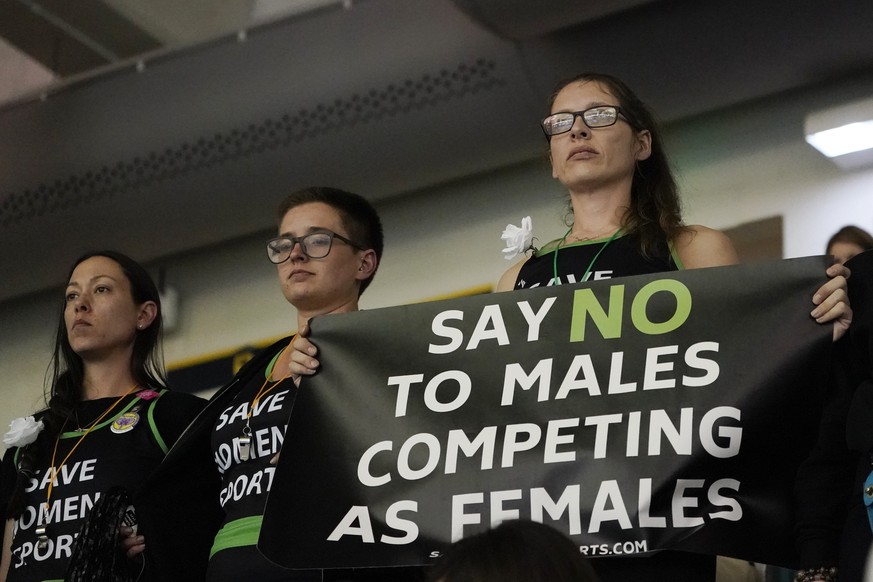Protesters, one holding a sign, stand as Pennsylvania transgender athlete Lia Thomas competes in the women&#039;s 200 freestyle final at the NCAA swimming and diving championships Friday, March 18, 20 ...