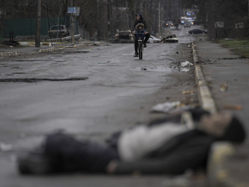 A man and child on a bicycle come across the body of a civilian lying on a street in the formerly Russian-occupied Kyiv suburb of Bucha, Ukraine, Saturday, April 2, 2022. (AP Photo/Vadim Ghirda)