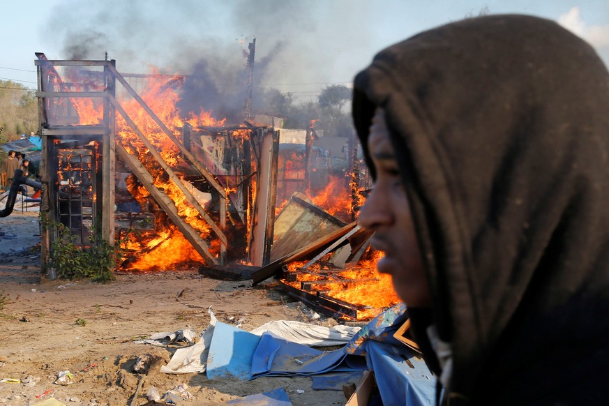 A migrant walks past a burning makeshift shelter set ablaze in protest against the dismantlement of the camp for migrants called the &quot;Jungle&quot; in Calais on the second day of their evacuation  ...
