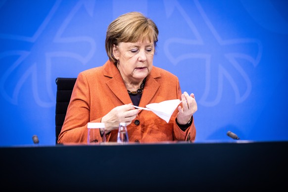 epa08880962 German Chancellor Angela Merkel takes off her face mask before speaking during a press conference after a video conference with German State Premiers about increased anti-coronavirus measu ...