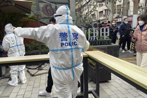 Ein Polizeibeamter in Schutzkleidung dirigiert Menschen, die einen Corona-Test machen möchten, Shanghai, China.