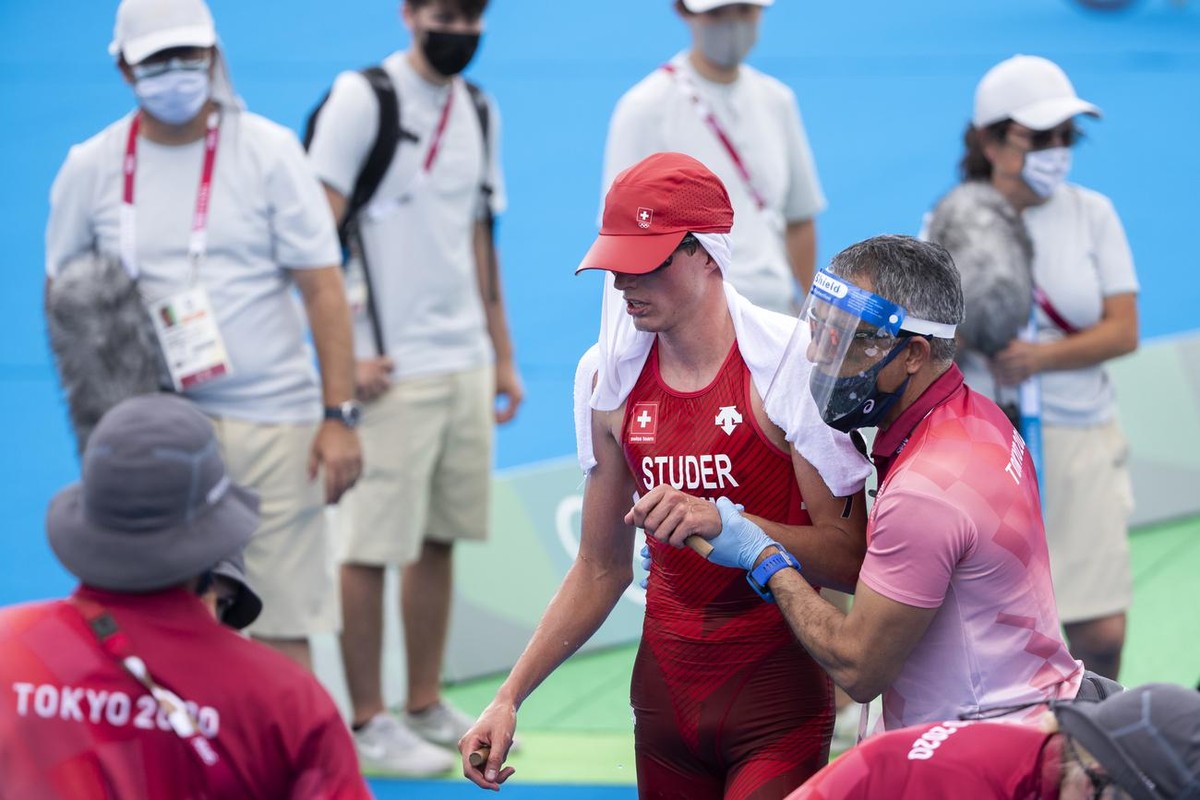 A medical staff member takes care of Switzerland's Max Studer in the finish area during the men's Individual Triathlon competition at the 2020 Tokyo Summer Olympics in Tokyo, Japan, on Monda ...