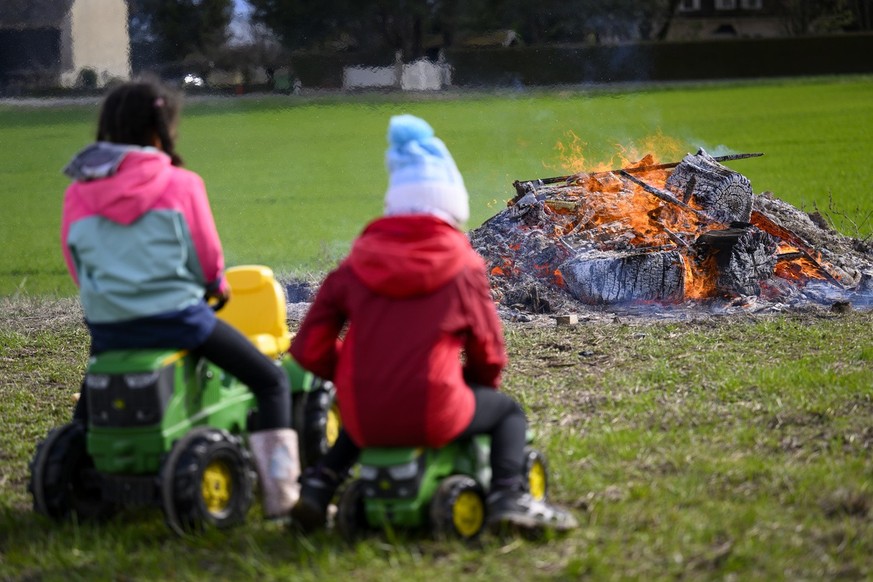 Kinder sitzen auf Miniaturtraktoren und beobachten das Feuer während der Aktion &quot;Protestfeuer für die Landwirtschaft&quot;, die von der Facebook-Gruppe &quot;Revolte agricole Suisse&quot; während ...