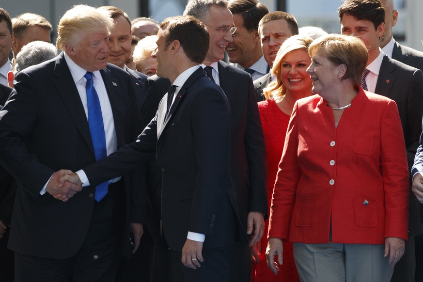 German Chancellor Angela Merkel watches as President Donald Trump shakes hands with French President Emmanuel Macron during a ceremony to unveil artifacts from the World Trade Center and Berlin Wall f ...