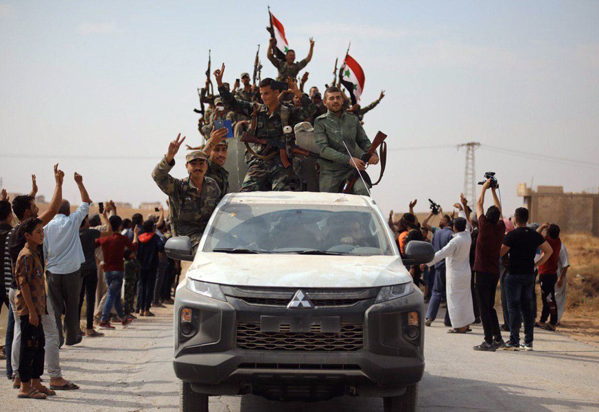 In this photo released by the Syrian official news agency SANA, people welcome Syrian troops as they enter the town of Ein Issa, north of Raqqa, Syria, Monday, Oct 14, 2019. Syrian troops moved east f ...