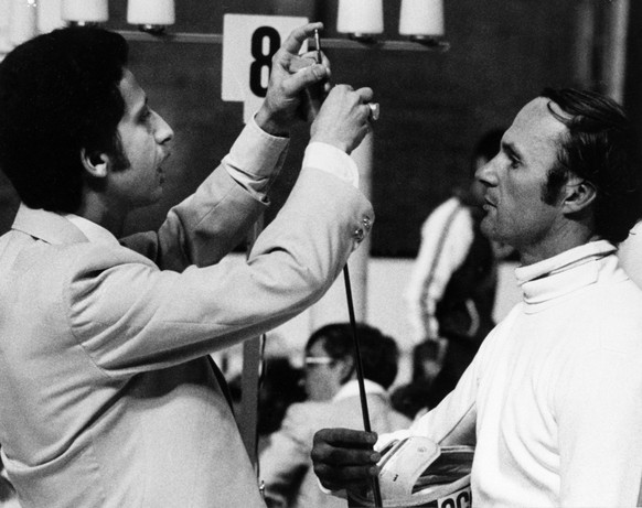 An unidentified fencing judge examines the weapon of Russian pentathlonist Boris Onischenko, July 19, 1976, after British competitors claimed there was something wrong with his sword. Onischenko was d ...