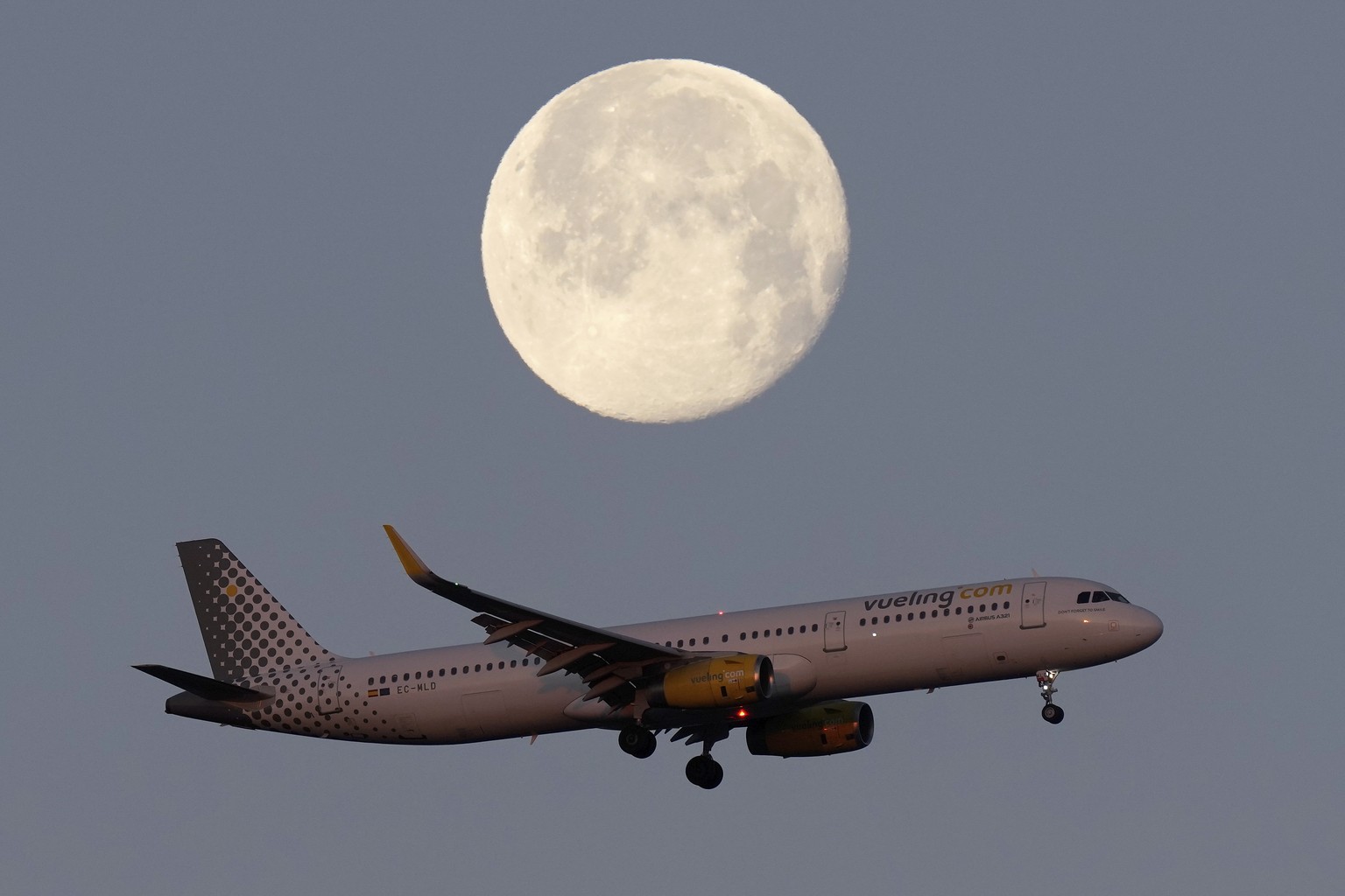 A Vueling Airbus A321 approaches for landing in Lisbon at sunrise, with the moon in the background, Tuesday, Feb. 7, 2023. (AP Photo/Armando Franca)