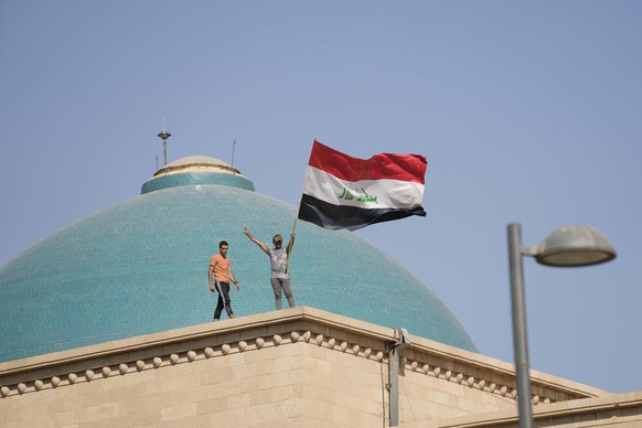 Supporters of Shiite cleric Muqtada al-Sadr wave a national flag from the roof of the Government Palace during a demonstration in Baghdad, Iraq, Monday, Aug. 29, 2022. Al-Sadr, a hugely influential Sh ...