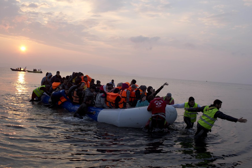 Helfer ziehen ein Boot mit Flüchtlingen an den Strand von Lesbos.