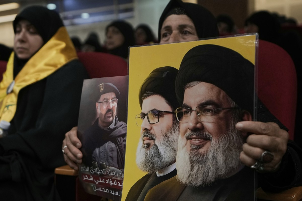 A woman holds photos of top Hezbollah commander Fouad Shukur, left, who was killed in an Israeli airstrike, Hezbollah's former leader Hassan Nasrallah, right, and his cousin and successor, Hashem ...