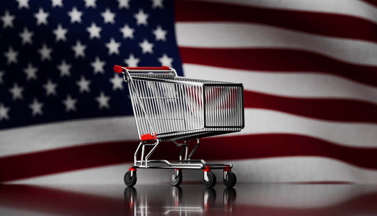 An engaging photograph featuring a shopping cart prominently placed in front of a large American flag, showcasing a shallow depth of field that emphasizes the cart while softly blurring the flag. This ...