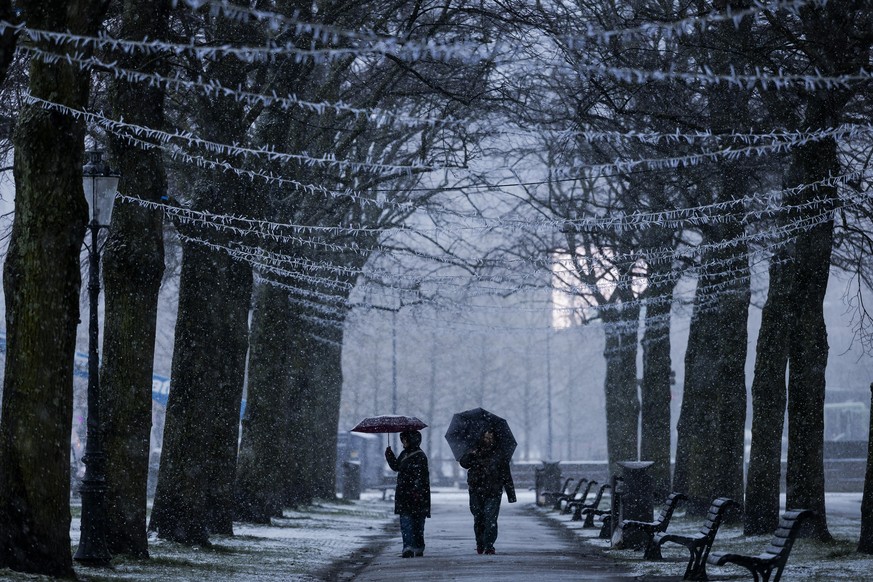 epa12625906 People walk through a winter shower with umbrellas in Amsterdam, The Netherlands, 04 January 2026. Showers of hail and snow are moving across the Netherlands. EPA/ROBIN VAN LONKHUIJSEN
