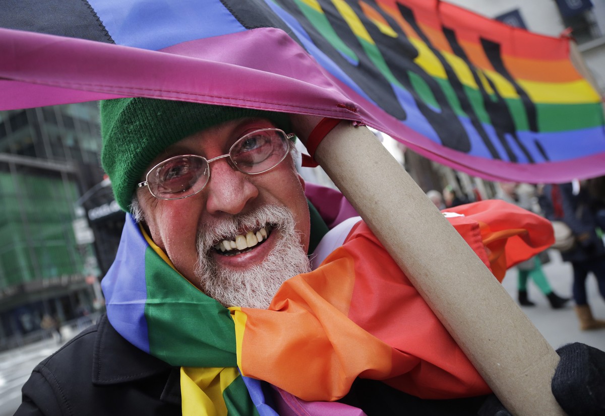 Artist Gilbert Baker, designer of the Rainbow Flag, is draped with the flag while holding a banner that reads "Boycott Homophobia" before the start of the St. Patrick's Day parade, Mond ...