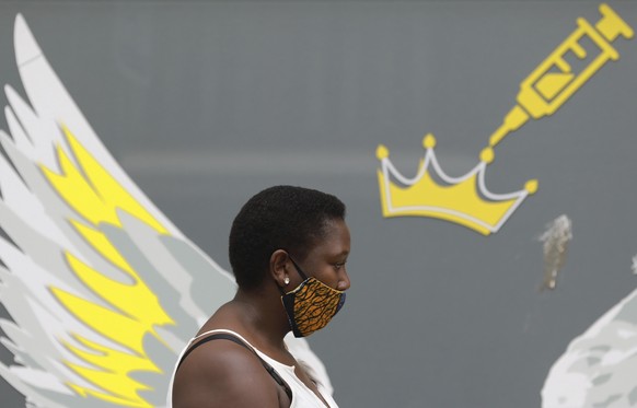 A woman wears a mask to protect against coronavirus as the passes a wall mural depicting a syringe , n Cape Town, South Africa, Thursday, Jan. 21, 2021. South Africa is preparing a hero‚Äôs welcome Mo ...