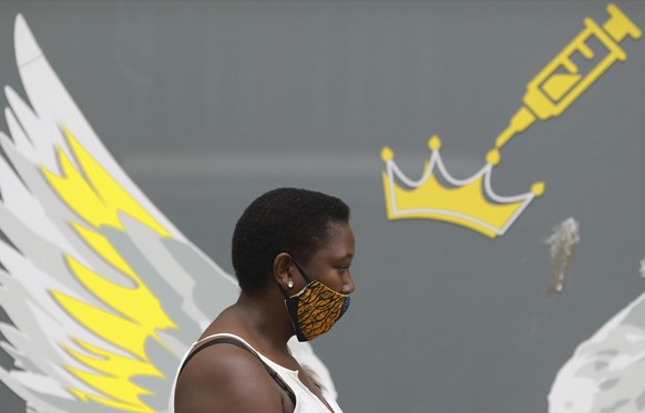 A woman wears a mask to protect against coronavirus as the passes a wall mural depicting a syringe , n Cape Town, South Africa, Thursday, Jan. 21, 2021. South Africa is preparing a heroÄôs welcome Mo ...