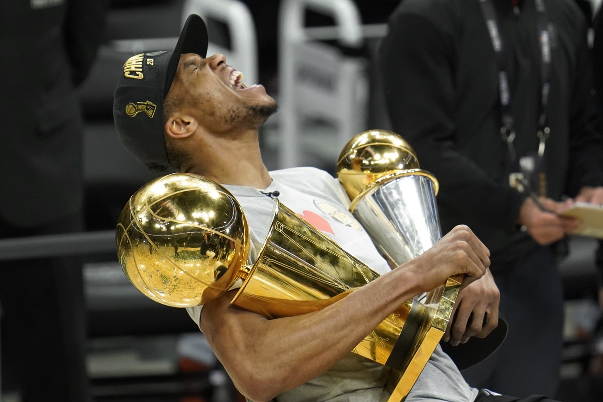 Milwaukee Bucks forward Giannis Antetokounmpo reacts while holding the NBA Championship trophy, left, and Most Valuable Player trophy after defeating the Phoenix Suns in Game 6 of basketball's NB ...