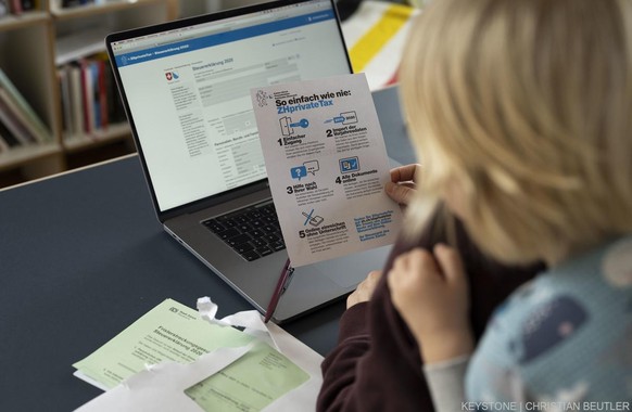 Eine Frau in Anwesenheit ihres Sohnes studiert in ein Infoblatt zur Einreichung Online-Steuererklaerung 2020 (ZHprivate Tax) des Kanton Zuerich, fotografiert am 25. Januar 2021 in Zuerich. (KEYSTONE/C ...