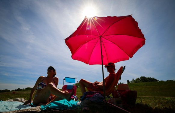 ARCHIV - 31.05.2023, Hamburg: Unter einem pinkfarbenen Sonnenschirm genie�en zwei Menschen den sonnigen Tag auf einer Wiese am Elbdeich bei Ochsenwerder. (zu dpa: �Hamburg bekommt eigene UV-Strahlen-M ...