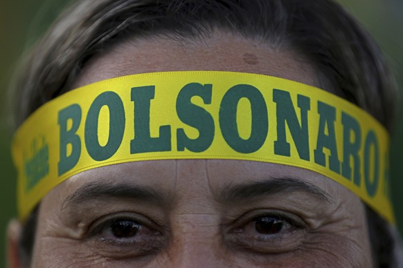 A supporter of presidential front-runner Jair Bolsonaro wears a headband supporting his candidate as he waits with others for election results outside the National Congress in Brasilia, Brazil, Sunday ...