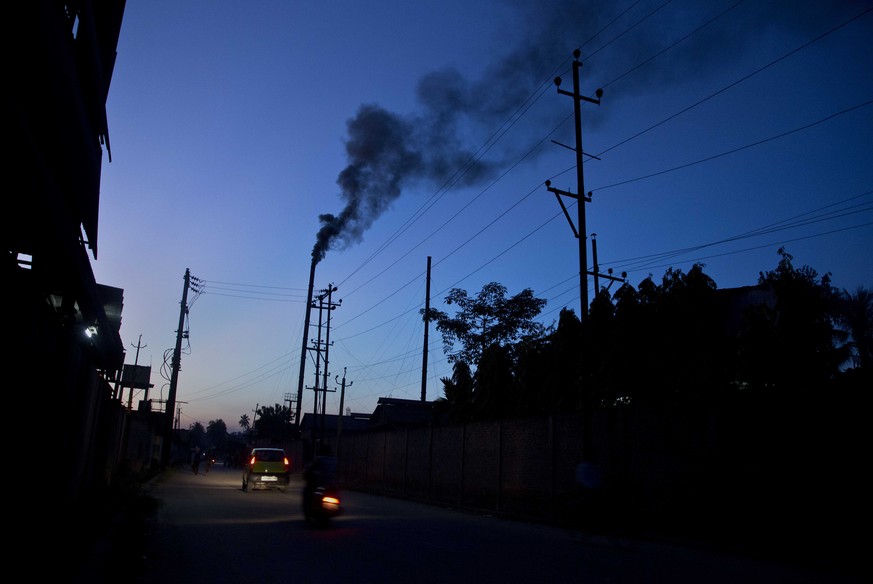 Traffic moves as smoke emits from the chimney of a factory on the outskirts of Gauhati, India, Sunday, Oct. 2, 2016. India is scheduled to deposit the ratification instruments of the Paris Agreement o ...