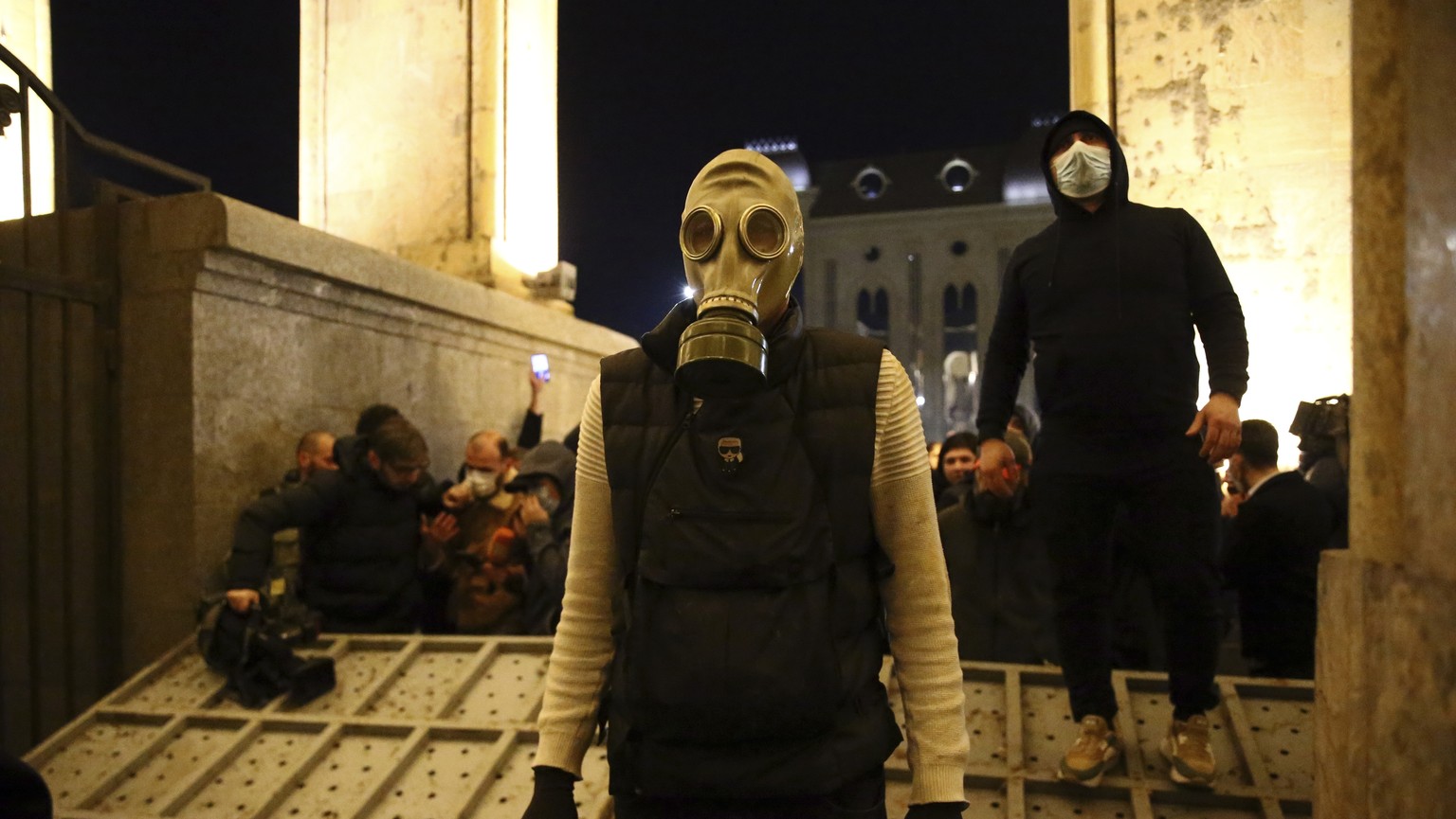 Protesters, one of them wearing a gas mask, gather at a broken security fence near the Georgian Parliament Building in Tbilisi, Georgia late Tuesday, March 7, 2023.  The Georgian authorities have used tears ...
