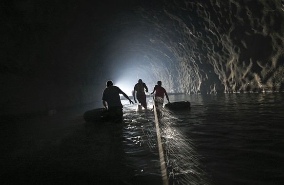 Men with inner tubes wade through an abandoned highway tunnel with the aid of a safety line as they work to repair a self-created water system in the Esperanza neighborhood of Caracas, Venezuela, on J ...