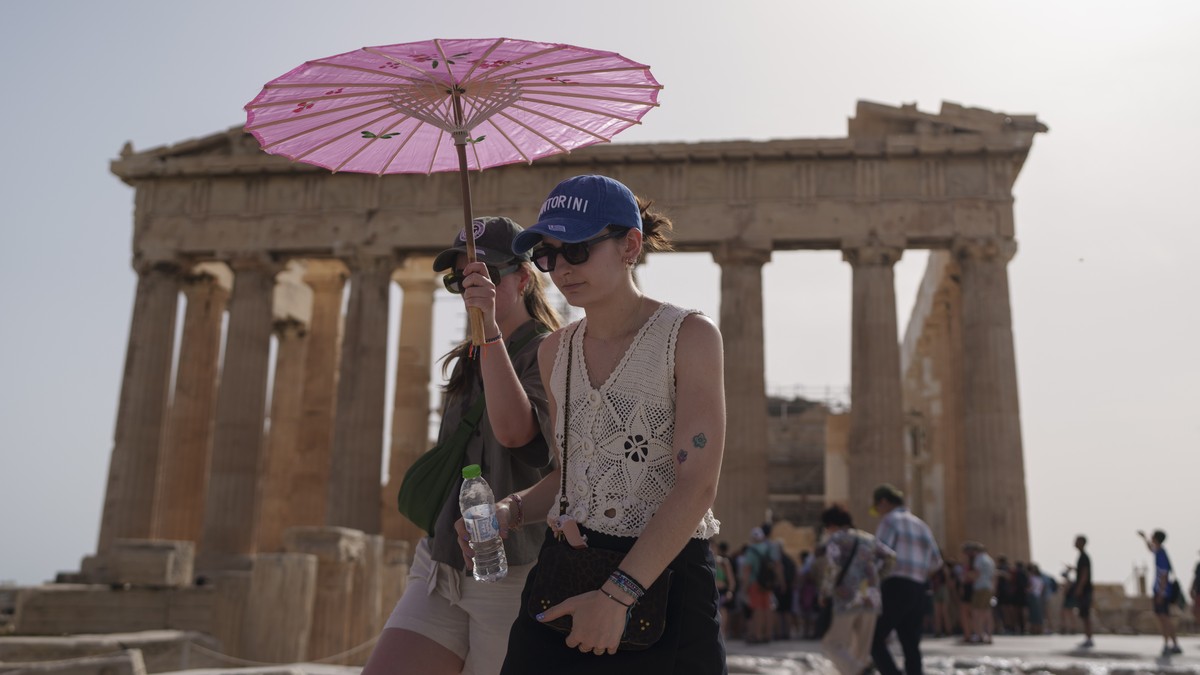 FILE - Tourists with an umbrella walk in front of the Parthenon at the ancient Acropolis in central Athens, June 12, 2024. June 2024 was the hottest June on record, according to Europe's Copernic ...