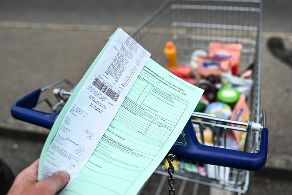 ARCHIV - 06.06.2020, Baden-W�rttemberg, Weingarten: ILLUSTRATION: Ein Kunde h�lt einen Ausfuhrschein samt Rechnung vor den Einkaufswagen. (zu dpa: �Schweiz senkt Grenze f�r steuerfreie Einfuhr�) Foto: ...
