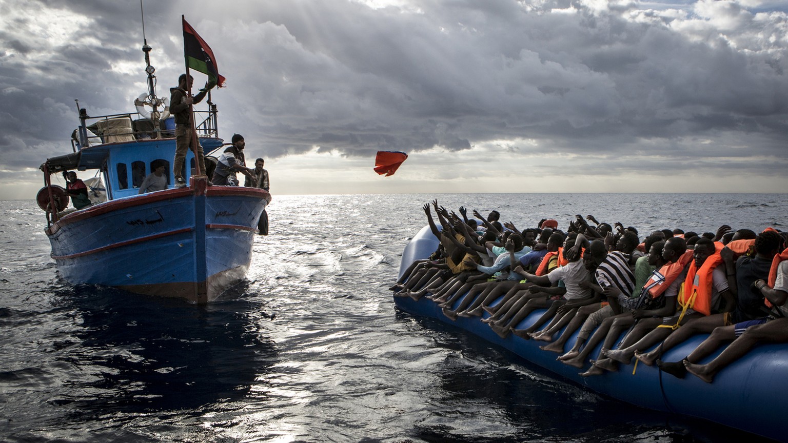 Libyan fishermen throw a lifejacket at a rubber boat full of migrants . Migrants are very often not given any life jackets or means of communication by their smugglers. More often than not they only h ...