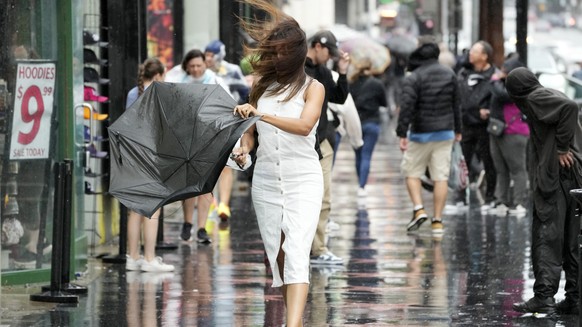 A pedestrian tends to a broken umbrella as she walks through wind and rain on Hollywood Boulevard during Tropical Storm Hilary, Sunday, Aug. 20, 2023, in Los Angeles. (AP Photo/Chris Pizzello)