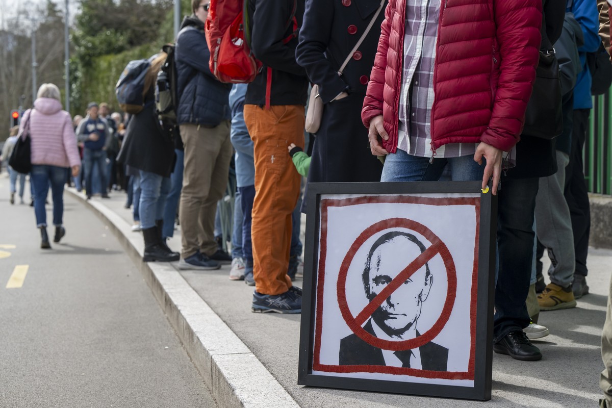 epa11225580 A protester holds a placard with a crossed-out picture of Russian President Vladimir Putin, as Russians living in Switzerland gather to protest with the slogan 'Noon against Putin ...