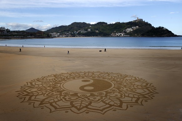 epa09885633 People walk along La Concha beach past a drawing made in the sand in San Sebastian, Basque Country, northern Spain, 12 April 2022. Forecasts are expecting light rainfalls during the day in ...