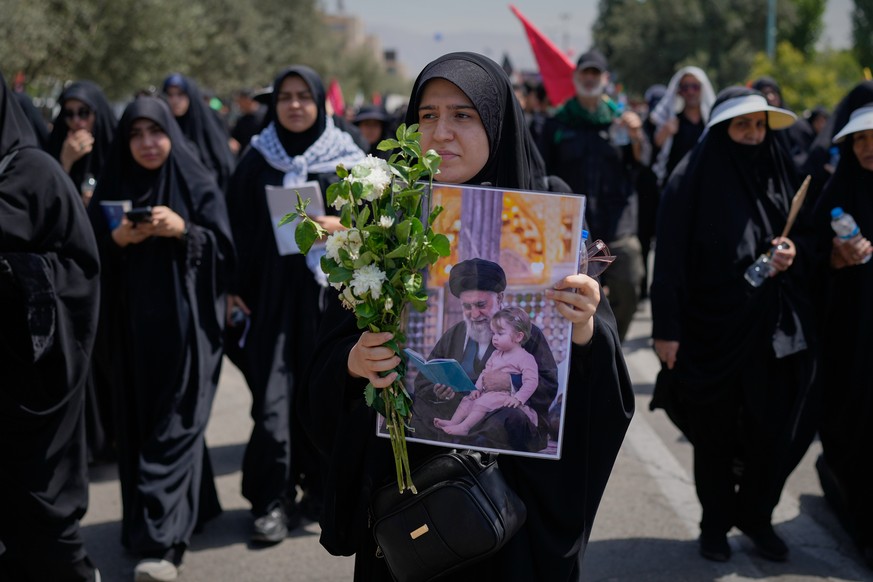 A mourner carries flowers and a portrait of slain Iranian Supreme Leader Ayatollah Ali Khamenei with a child as she walks toward the Imam Khomeini Mosalla Grand Mosque before the funeral ceremonies fo ...