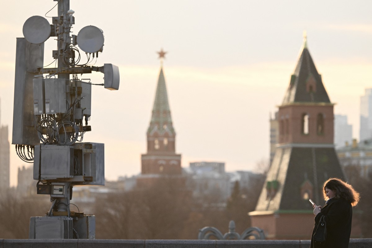 A woman uses her smartphone as she walks on the Moskvoretsky bridge past a cell tower in central Moscow on March 17, 2026. (Photo by Igor IVANKO / AFP)