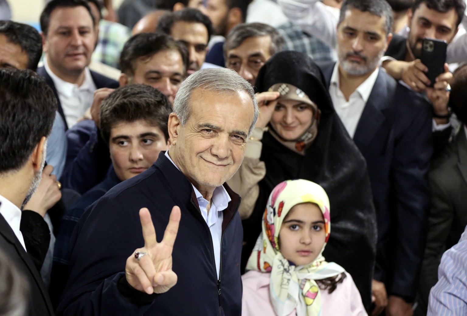epa11442776 Iranian reformist presidential candidate Masoud Pezeshkian (C) flashes a victory sign as he arrives to cast his vote at a polling station during the presidential election in Tehran, Iran,  ...