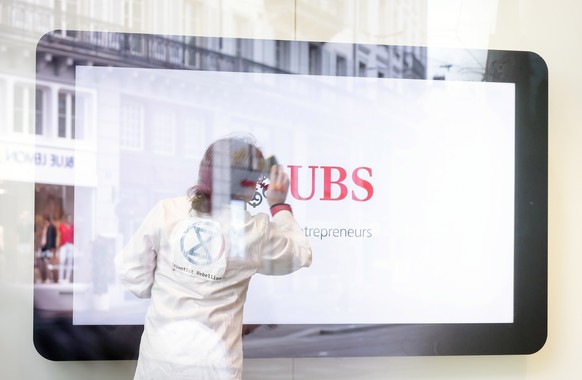 epa10619142 An activist of Scientist Rebellion cleans symbolically a screen inside a branch of Swiss Bank UBS at Paradeplatz during a protest against fossil fuel investments, in Zurich, Switzerland, 1 ...