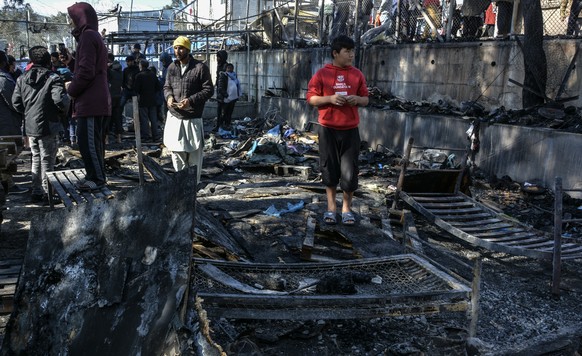 Migrants stand on a burned container home in Moria refugee camp on the northeastern Aegean island of Lesbos, Greece, Monday, March 16, 2020. The Fire Service said a migrant, who was not further identi ...