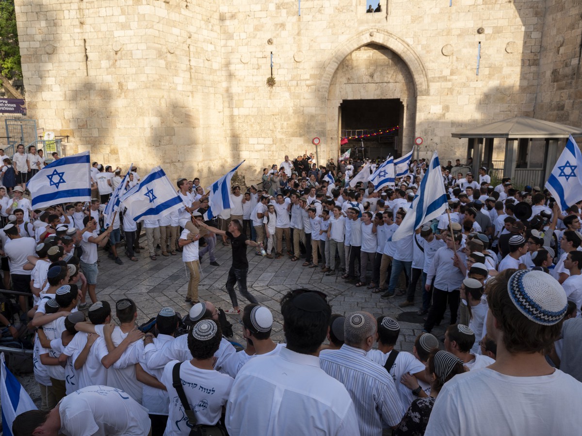 epa07620659 Right-wing Israeli youth dance with Israeli flags as they march into the Damascus Gate (behind) in East Jerusalem and enter the Old City's Muslim Quarter as they make their way to the ...